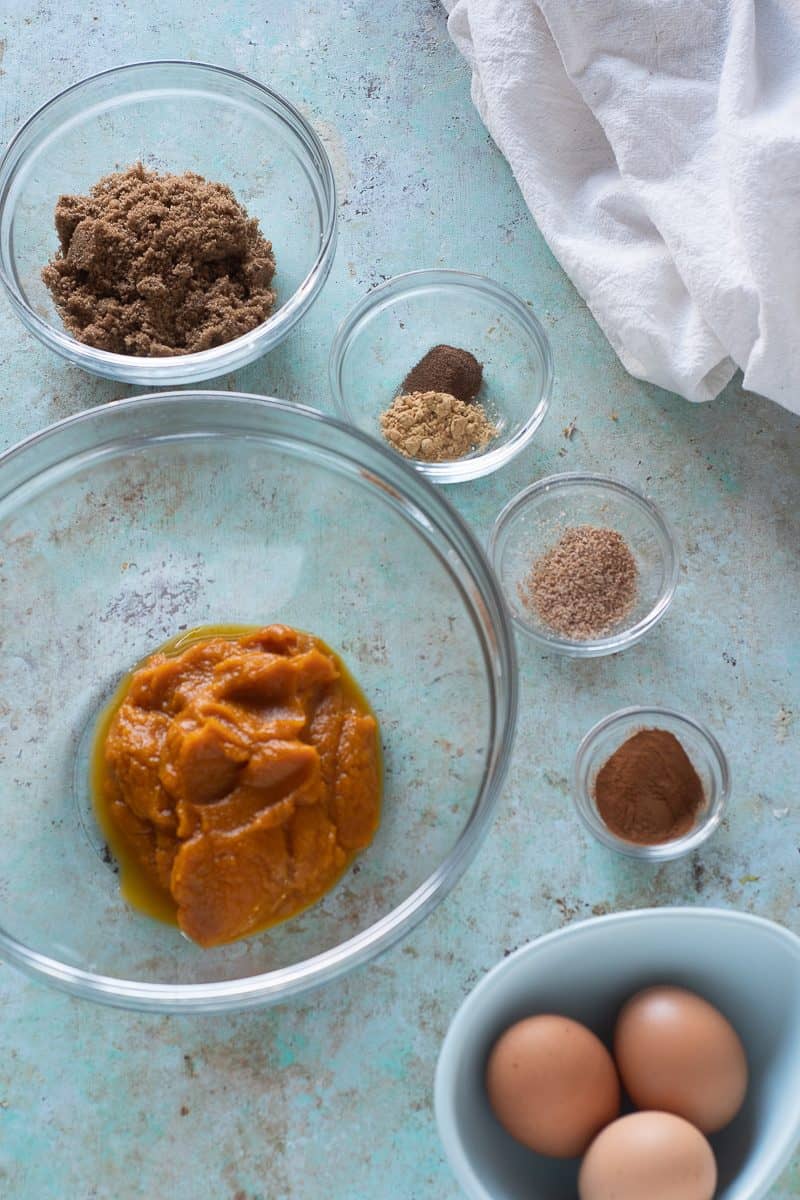 Pumpkin puree, dark brown sugar, ground ginger, allspice, nutmeg, cinnamon, and three eggs in bowls