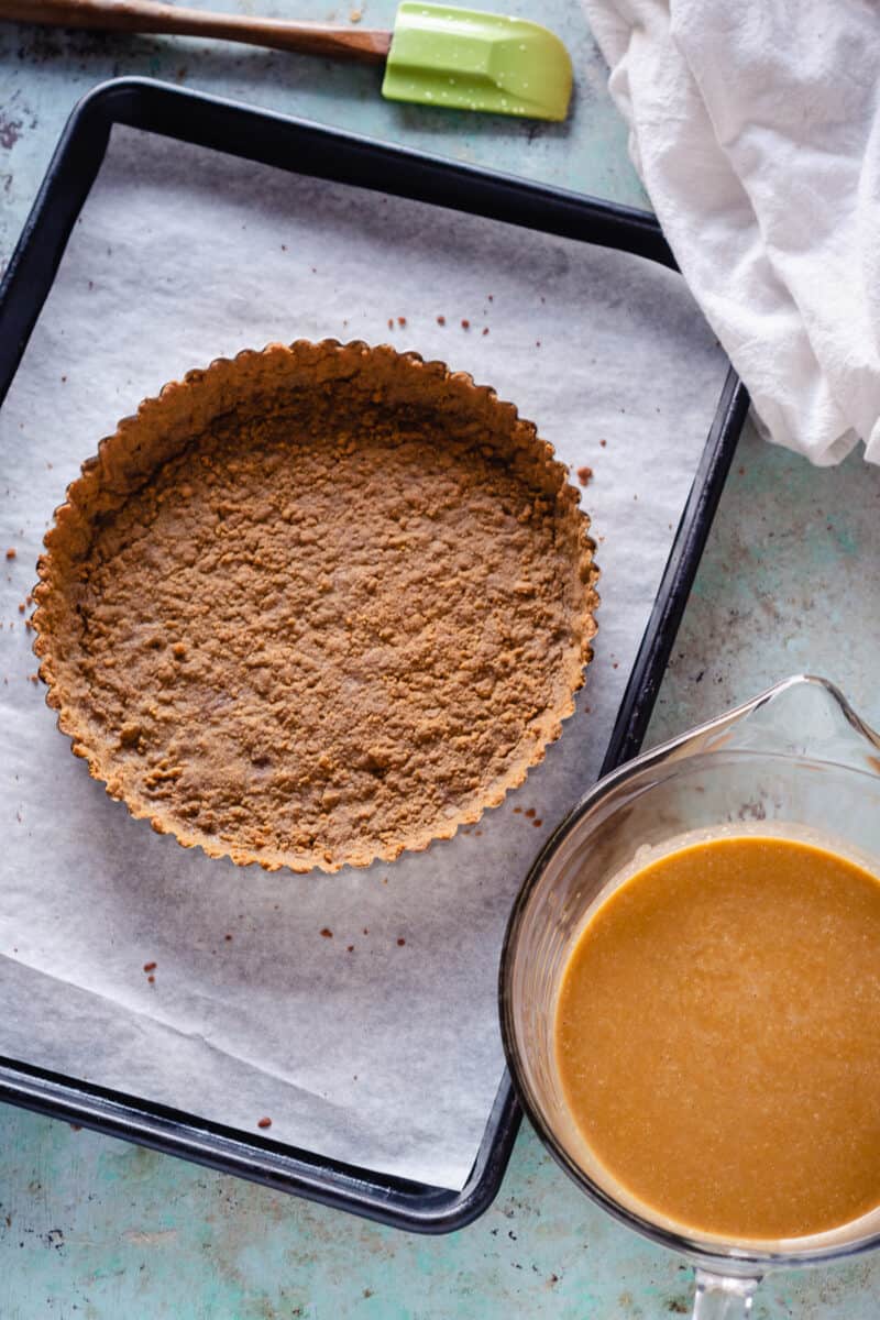 Gingersnap tart crust on a sheet pan with caramel pumpkin tart filling in a bowl