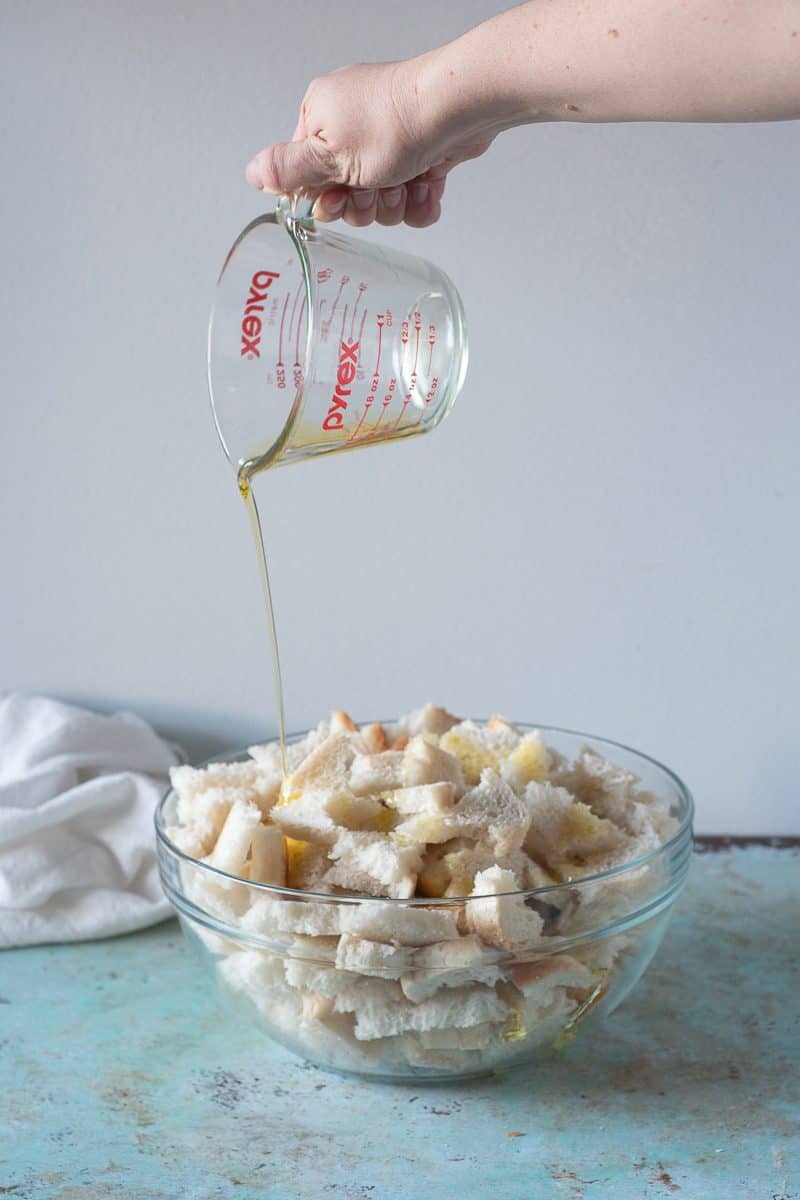 Torn bread pieces in a bowl being drizzled with olive oil