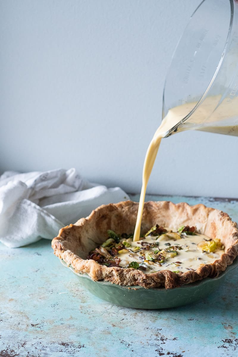 Pouring custard filling over bacon and Brussels sprouts into a pie crust