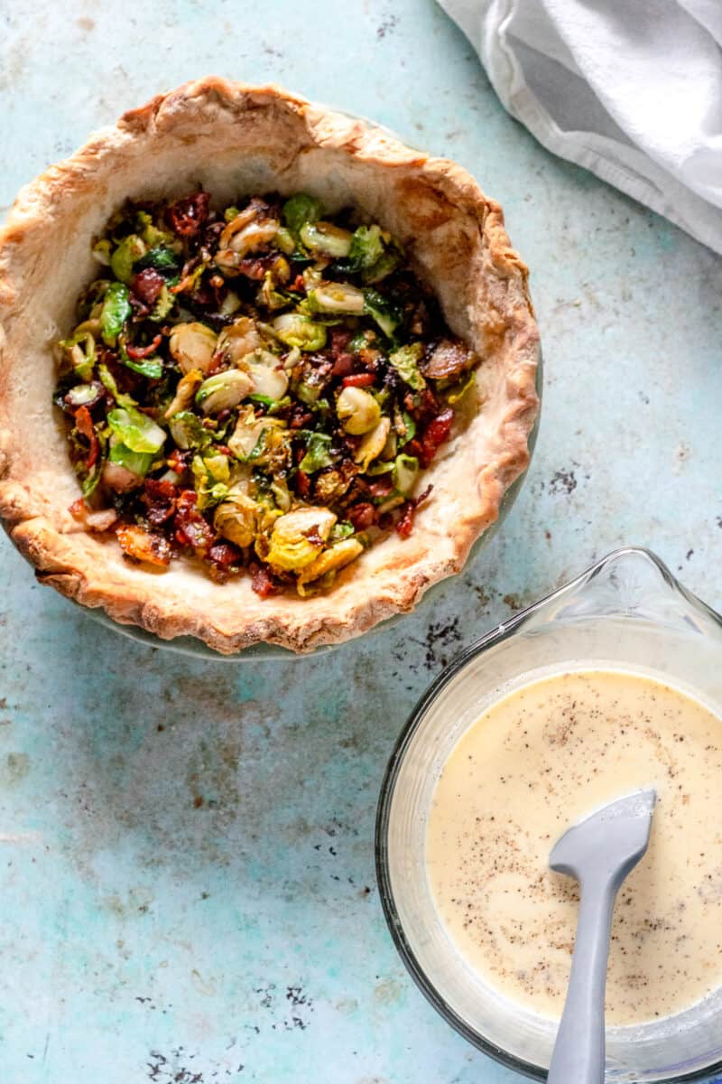 Bacon and Brussels sprouts in pie shell with egg mixture in a bowl nearby