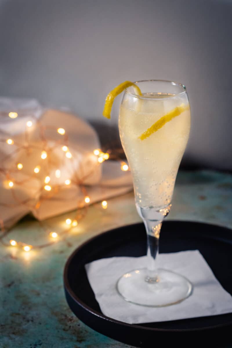 French 75 cocktail in a glass with a lemon garnish with twinkling lights behind it