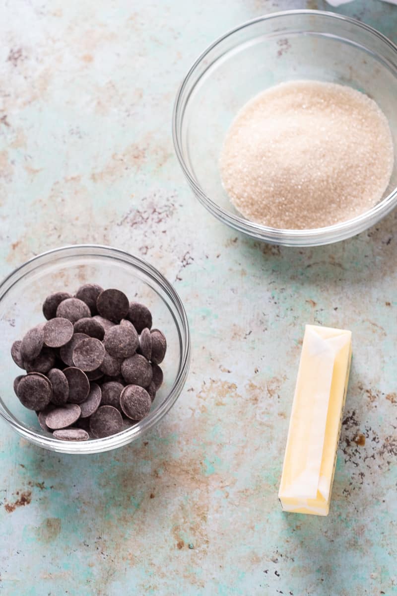 Bittersweet chocolate in a bowl, sugar in a bowl, a stick of butter