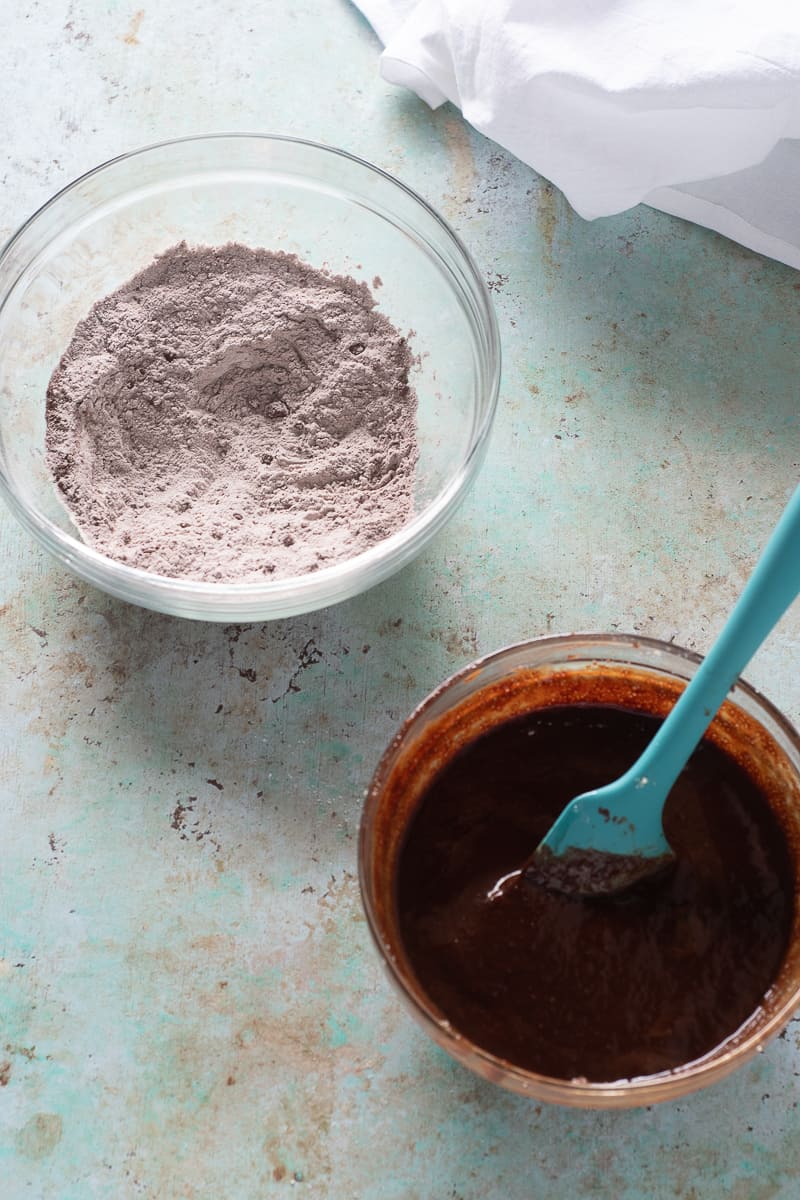 A bowl of flour, cocoa powder, and salt next to a bowl of melted chocolate, butter, sugar, eggs, and vanilla