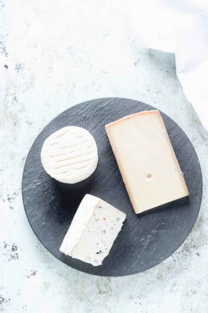 A triple creme cheese, a wedge of semi-hard cheese, and a wedge of blue cheese