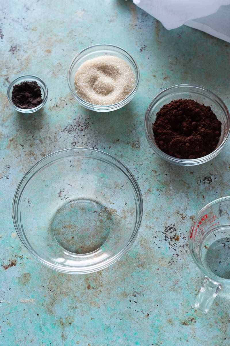 Bowls of espresso powder, sugar, and cocoa powder next to a measuring cup with water