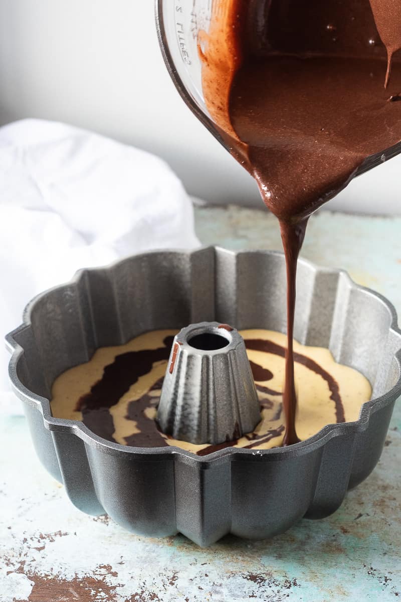 Adding layers of chocolate cake batter to orange olive oil cake batter in a Bundt pan