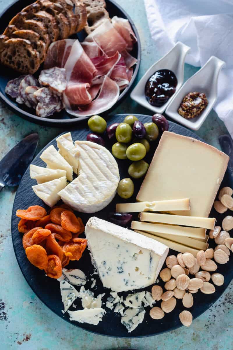 Cheese and charcuterie on a slate board with olives, apricots, and almonds