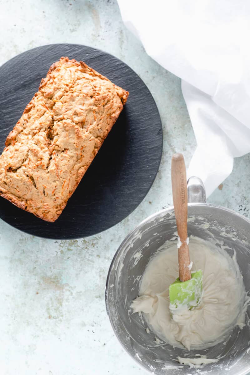 Carrot loaf cake with cream cheese frosting in a bowl next to cake