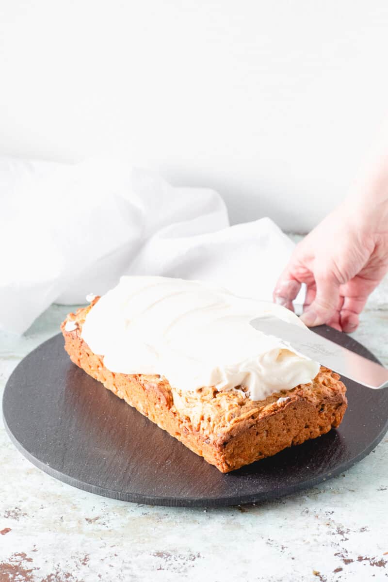 Hand spreading cream cheese frosting on carrot loaf cake