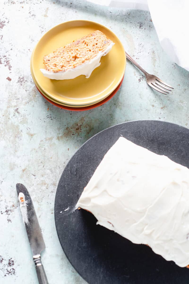 Slice of carrot loaf cake on a plate, with the rest of the loaf nearby