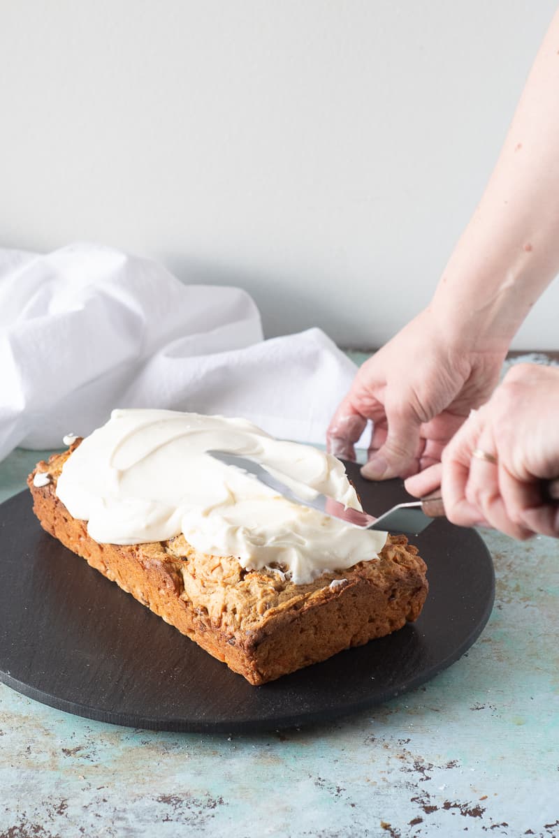 Spreading cream cheese frosting on carrot loaf cake