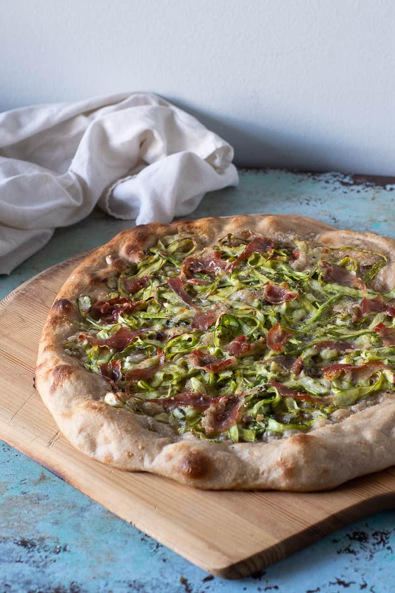 Asparagus Pizza with Prosciutto on a wooden peel, side view