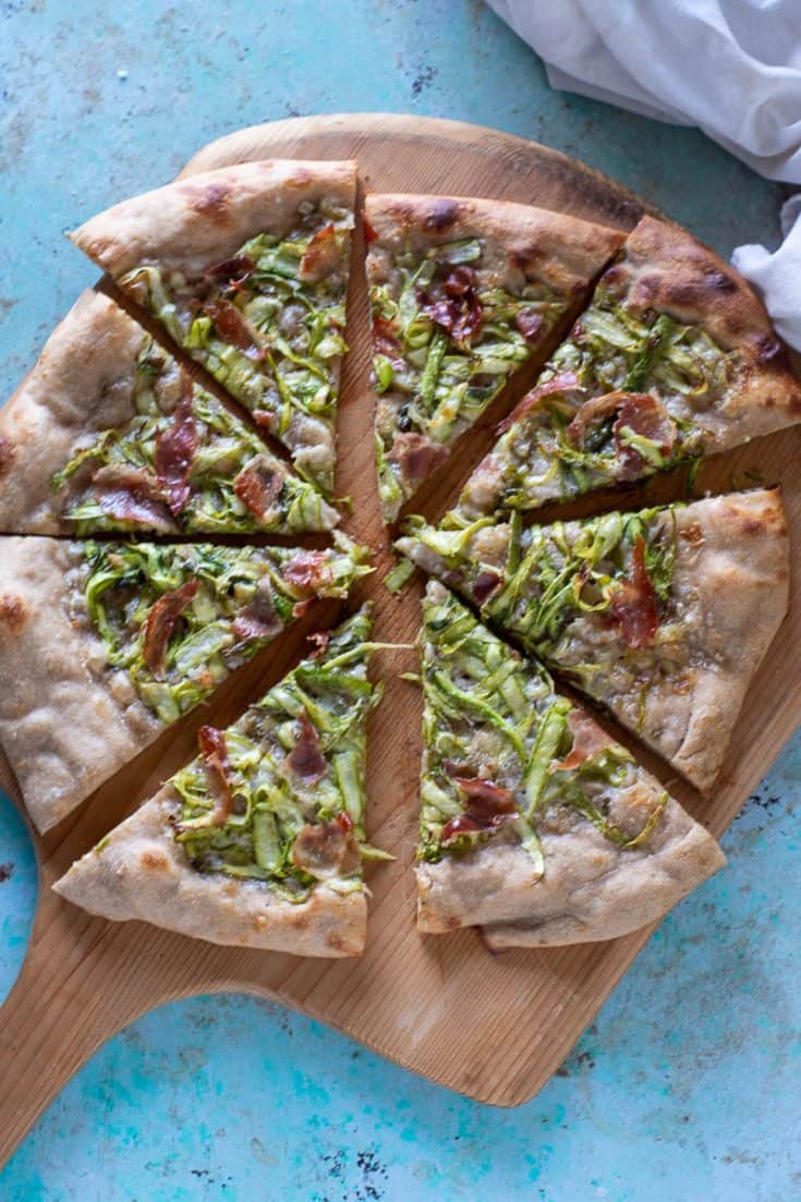 Sliced asparagus and prosciutto pizza on a wooden peel