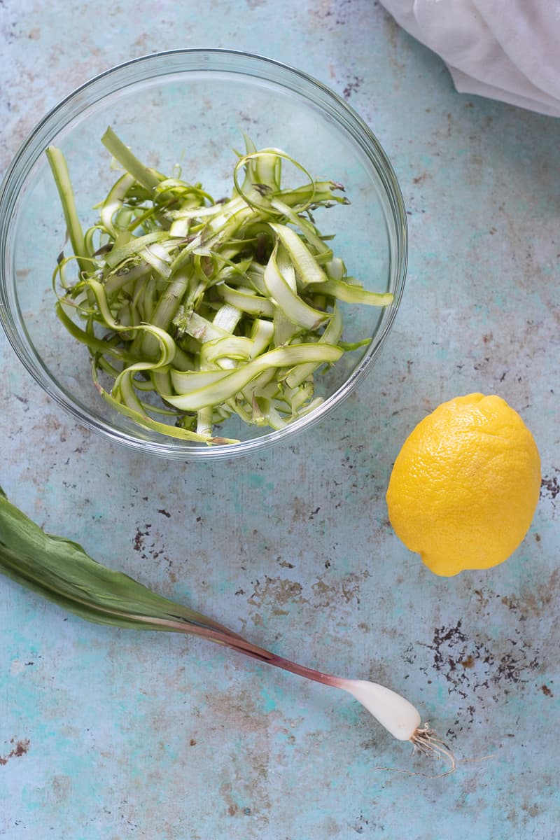 Shaved asparagus in a bowl, a lemon, and a ramp (wild onion)
