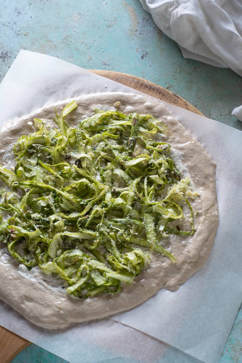 Shaved asparagus on unbaked pizza dough on parchment paper