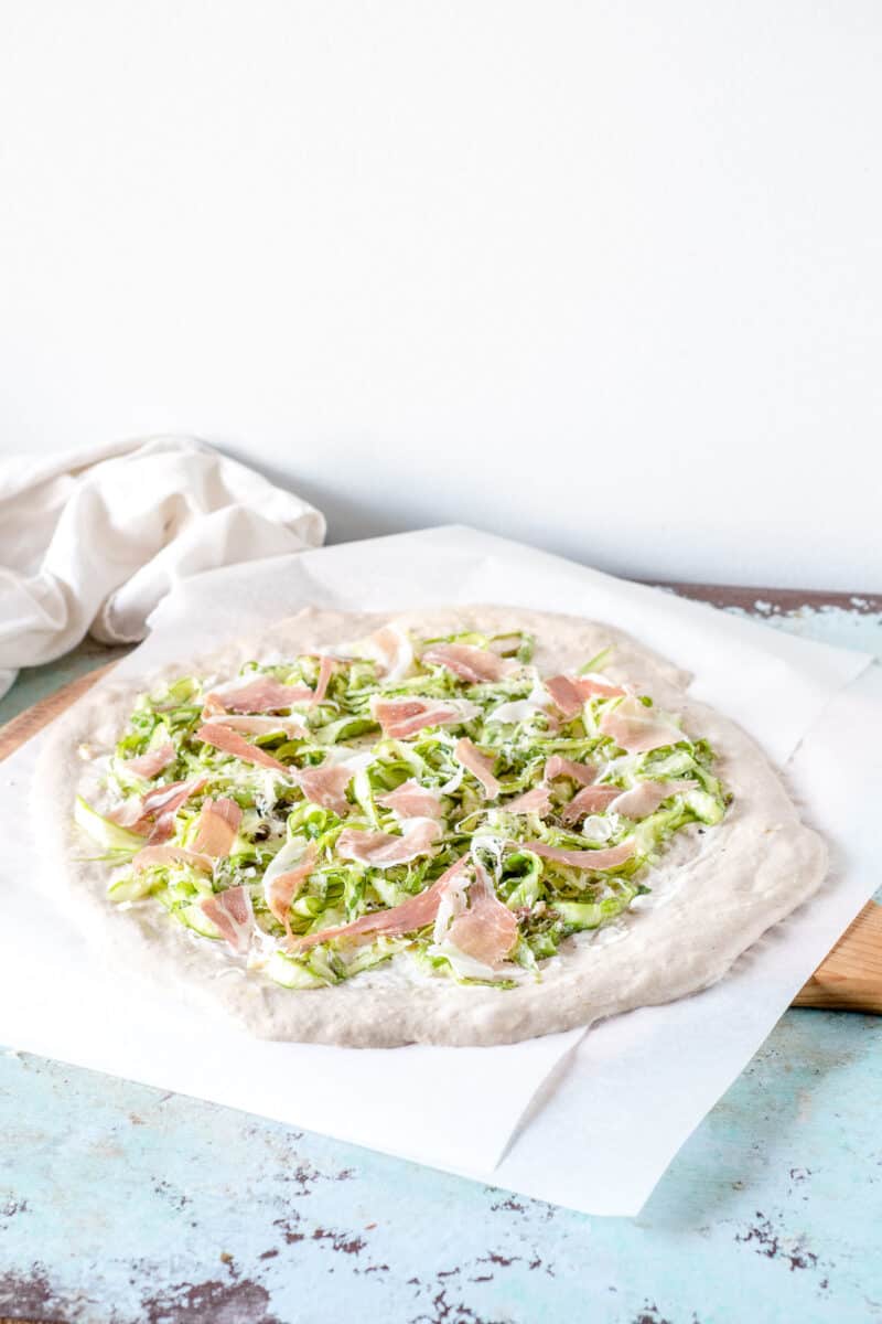 Pizza dough topped with shaved asparagus and prosciutto