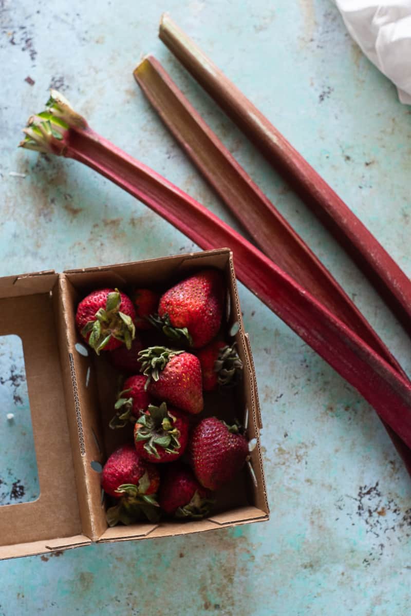 Strawberries in a cardboard containter next to three stalks of rhubarb