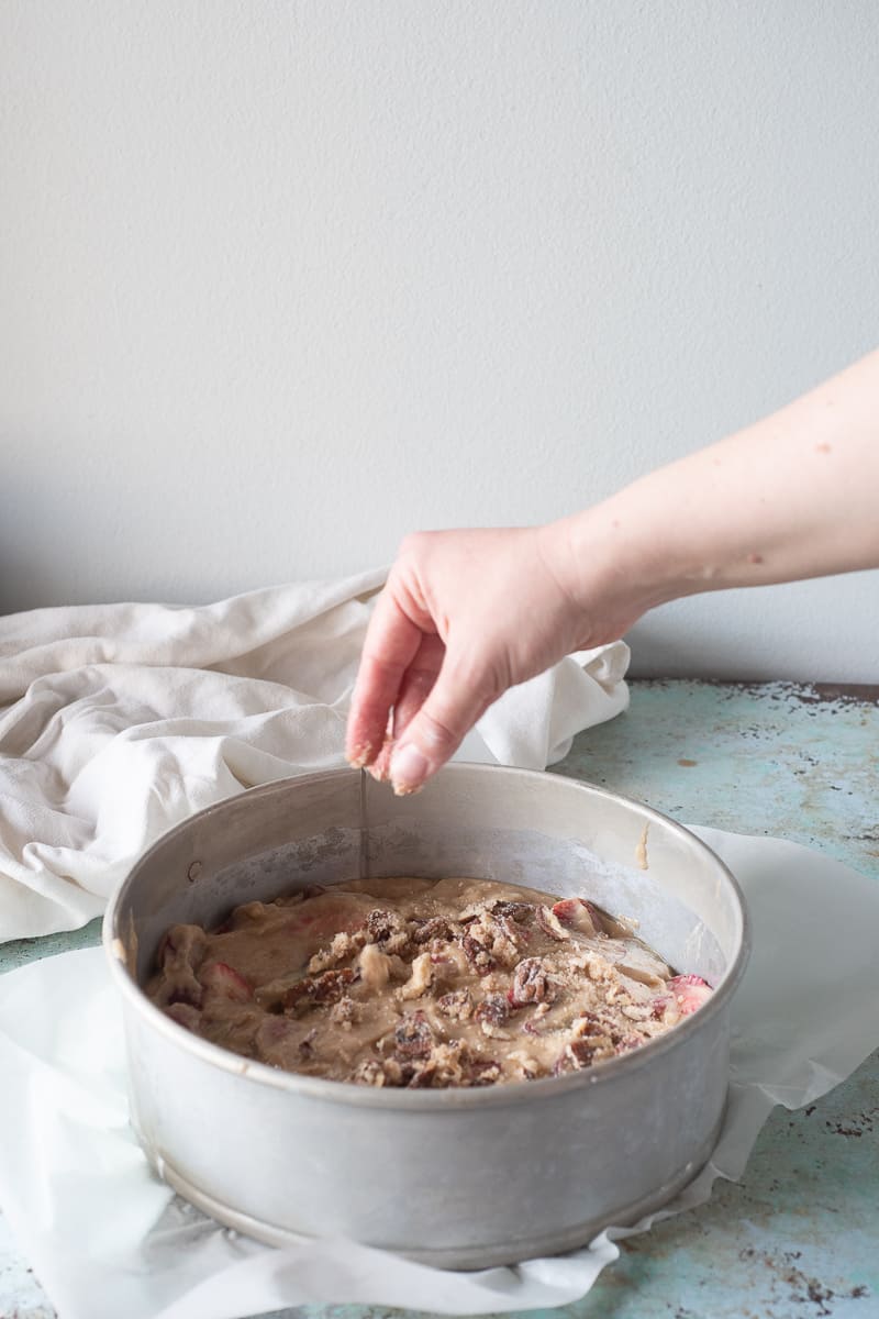 Sprinkling pecan streusel over the strawberry rhubarb buckle batter in a springform pan