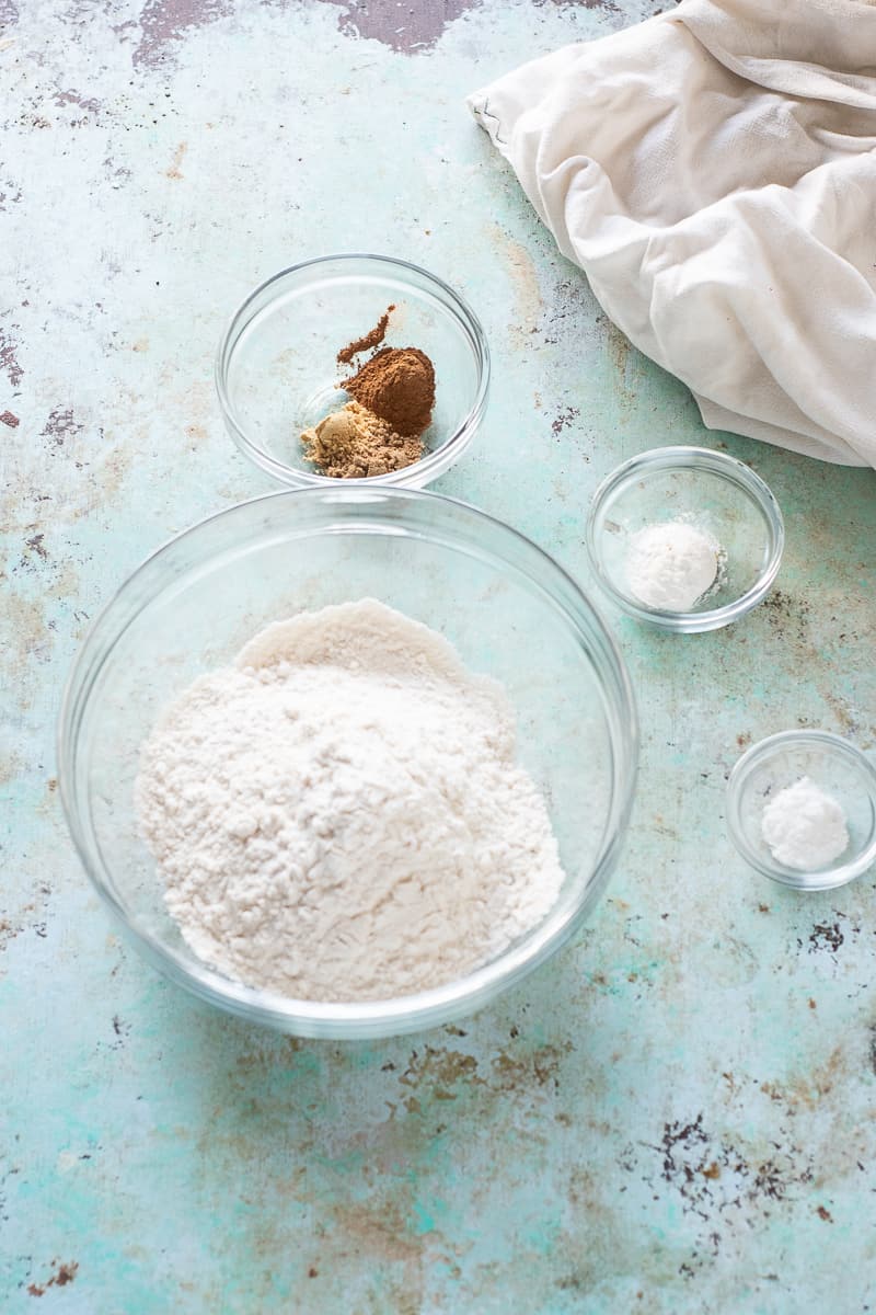 Flour in a bowl next to bowls of baking powder, baking soda, and cinnamon, coriander, and ginger