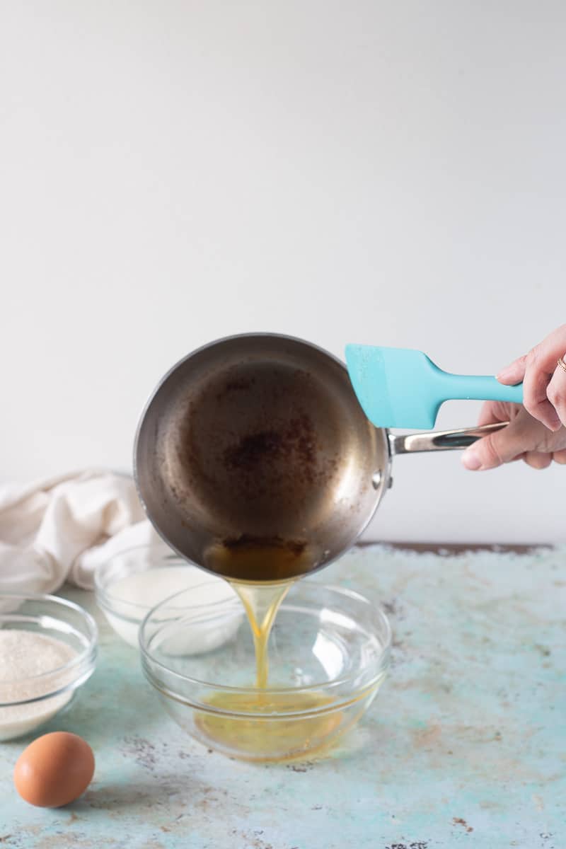 Pouring melted browned butter from a saucepan to a glass mixing bowl, an egg sits in the foreground