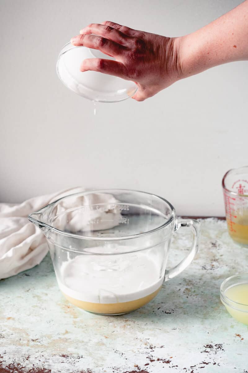 Hand pouring coconut milk into a mixing bowl with sweetened condensed coconut milk