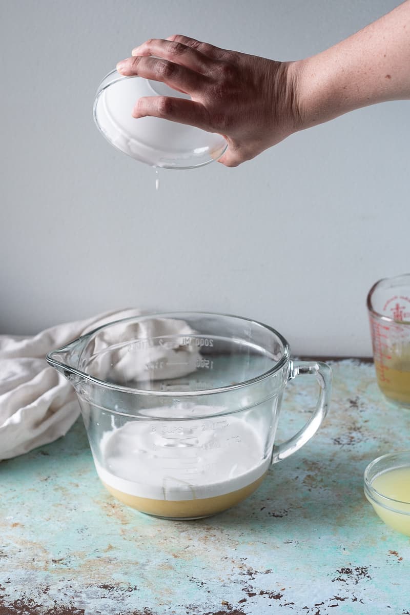 Hand pouring coconut milk into a mixing bowl with sweetened condensed coconut milk