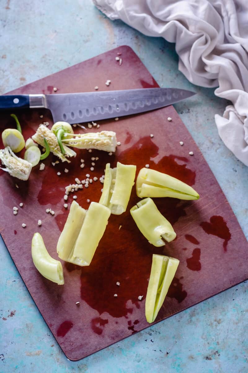 Banana peppers, de-seeded, on a cutting board with a knife