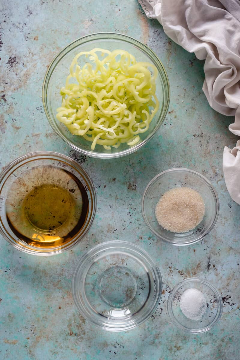 Sliced banana peppers in a bowl, champagne vinegar, sugar, water, and salt in bowls