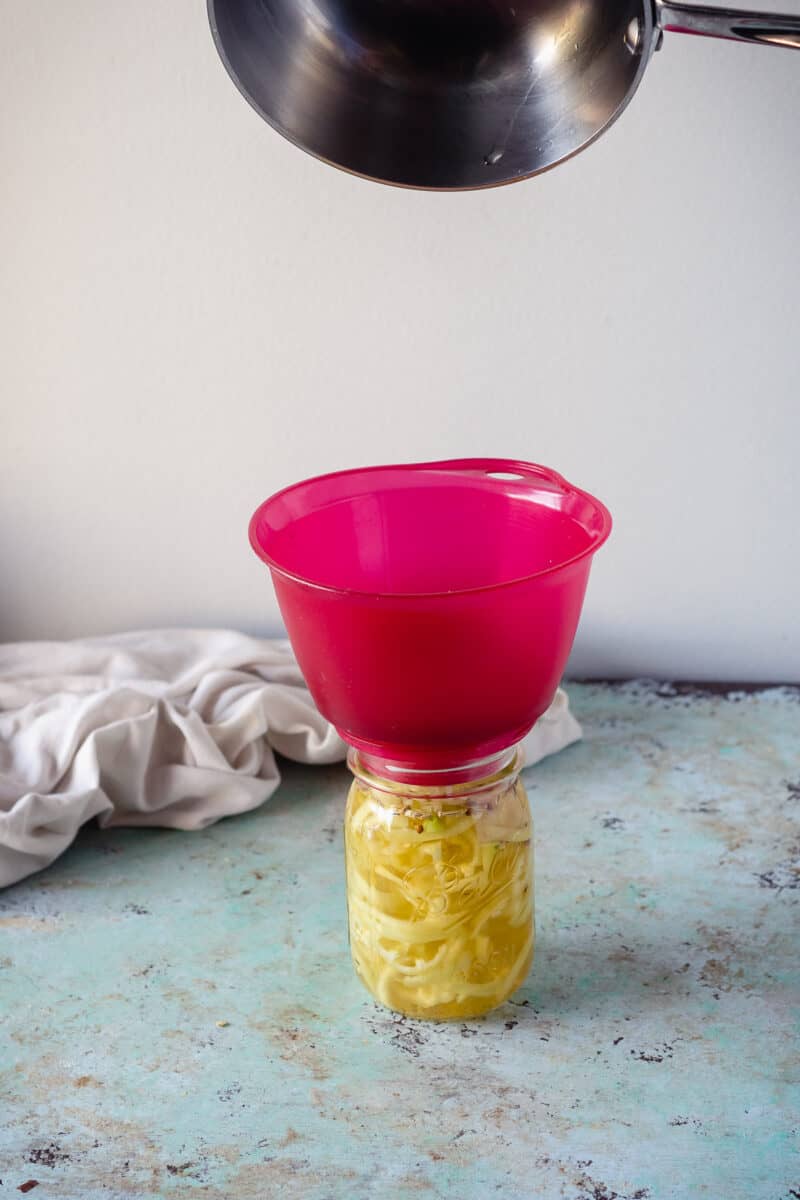 Pan pouring brine over banana peppers in a jar