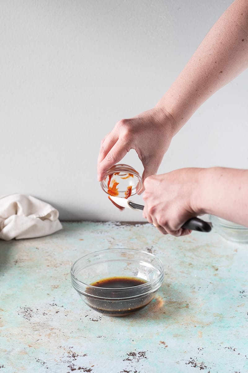 Hands scraping sriracha into a soy sauce mixture in a bowl