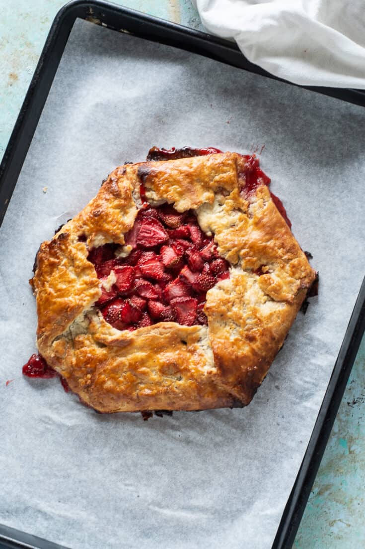 Strawberry galette on parchment paper on a sheet pan, overhead view, vertical