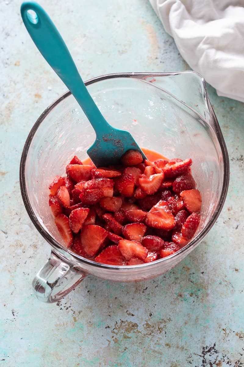 Strawberries macerated with sugar, tapioca starch, and lemon juice in a bowl with a spatula, overhead view