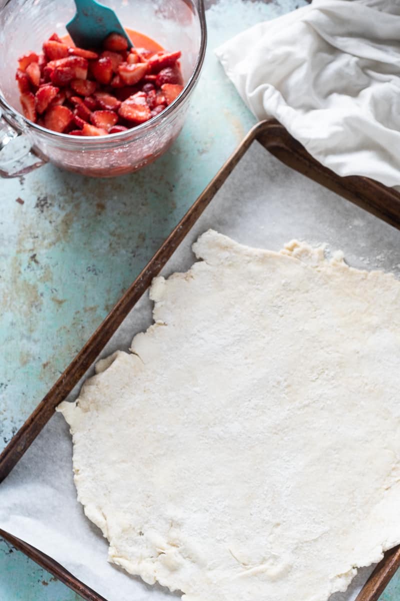 Rolled out galette dough on a sheetpan with strawberry filling in a bowl alongside