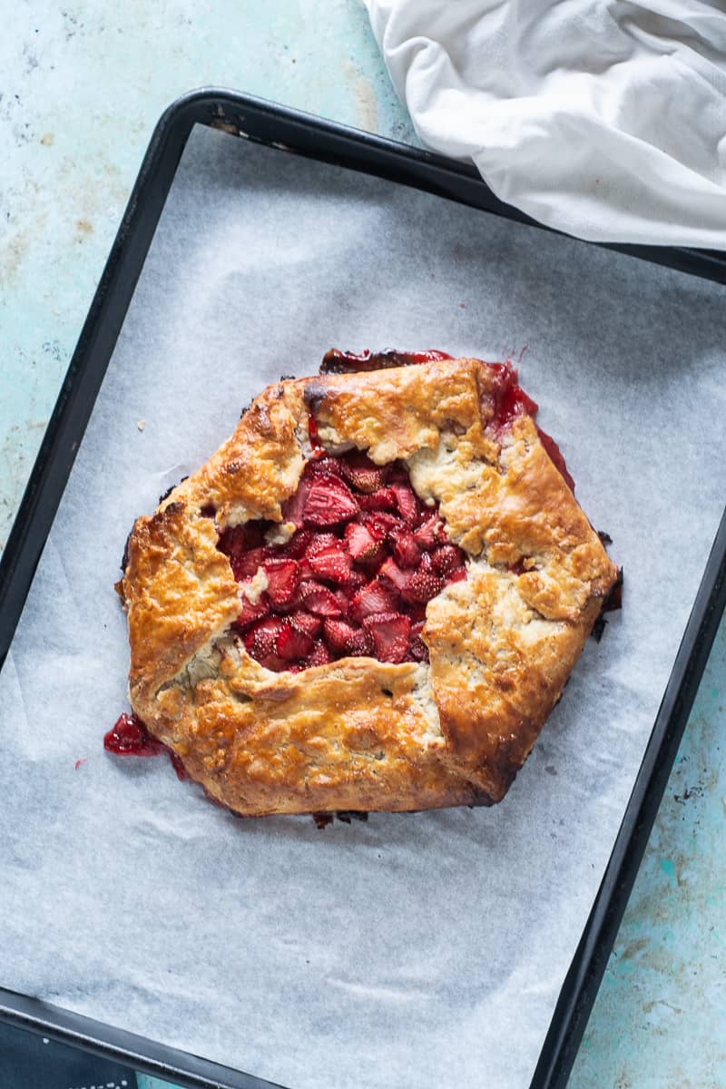 Finished strawberry galette on parchment on a sheet pan, overhead shot, vertical