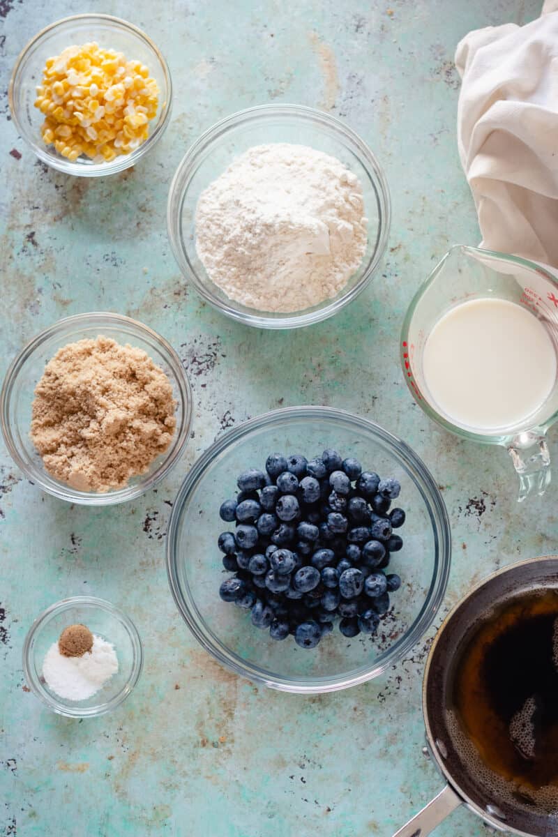 Bowls of sweet corn kernels, flour, whole milk, blueberries, brown sugar, baking soda, salt, and coriander