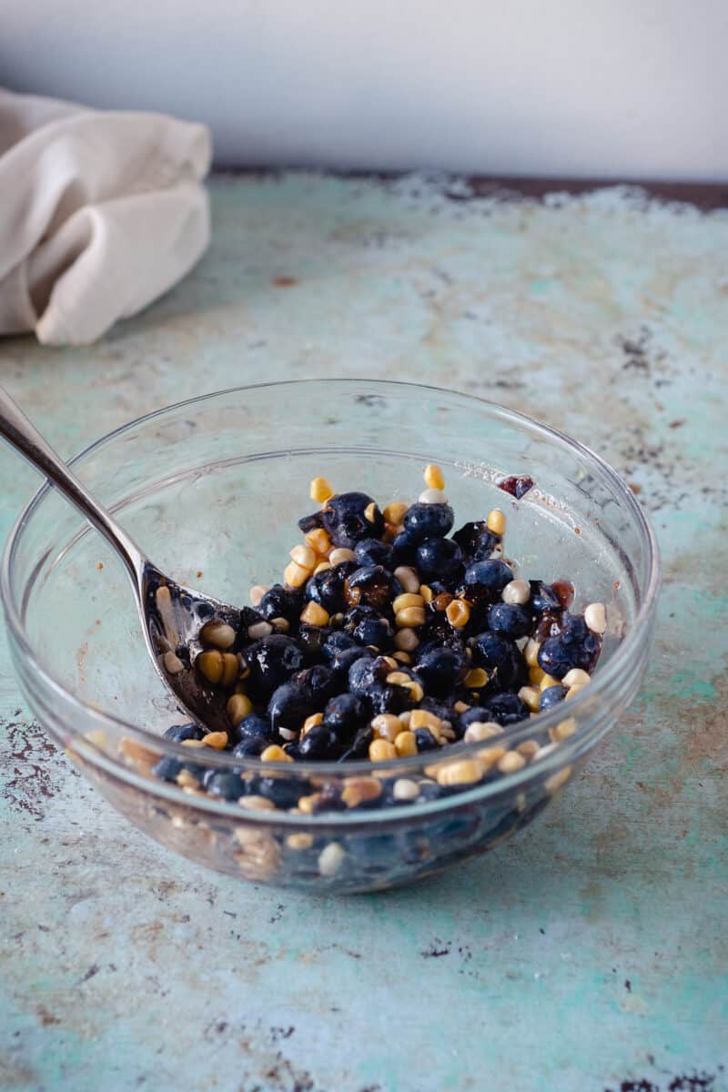 Blueberries and sweet corn gently mashed with brown sugar in a bowl
