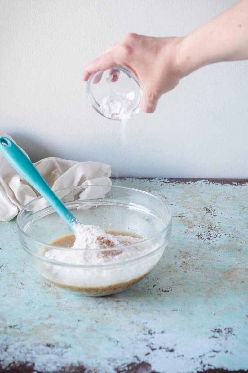 Hand adding baking soda to a bowl of batter