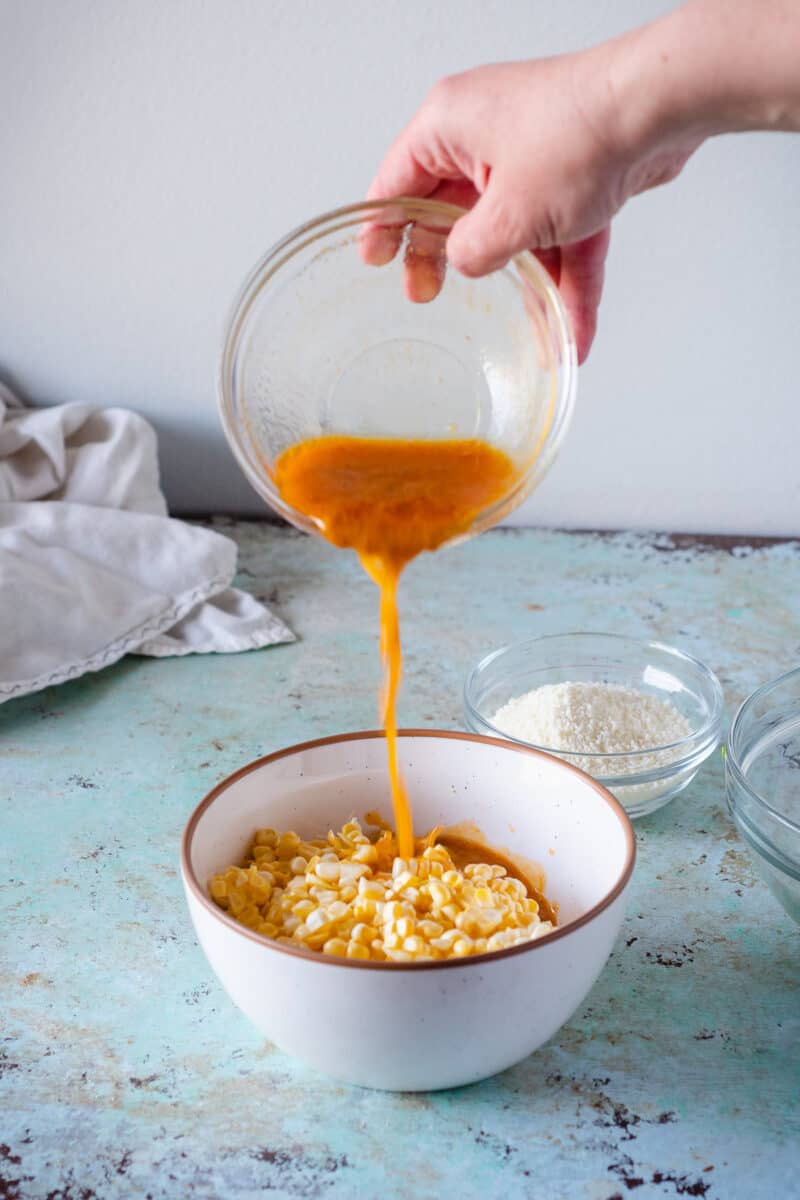 Corn kernels in a white bowl with a hand pouring miso lime butter over them