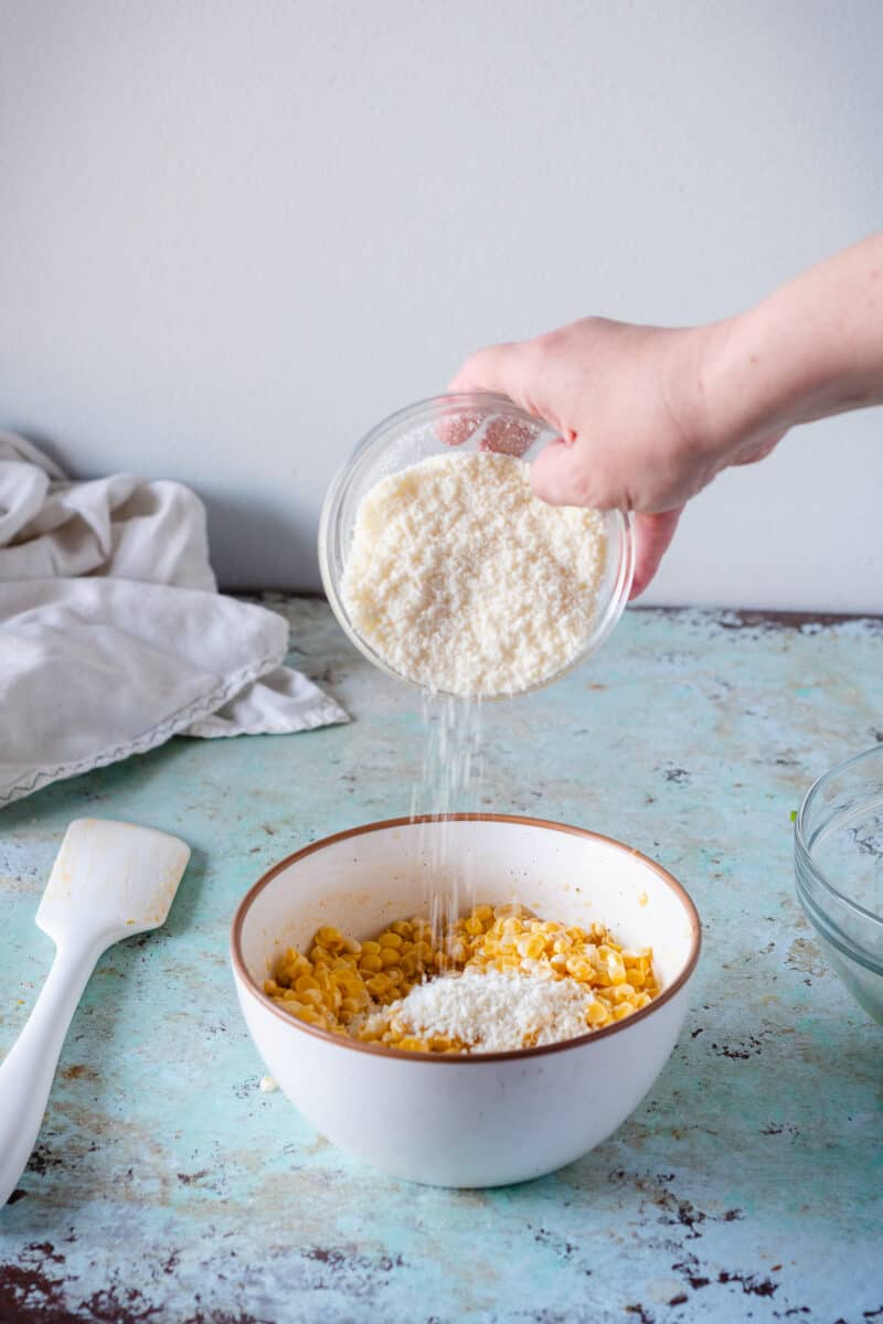 A bowl of corn kernels tossed with miso lime butter with grated cotija cheese being sprinkled on top