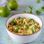 Corn with miso lime butter in a white bowl with limes and cilantro in the background