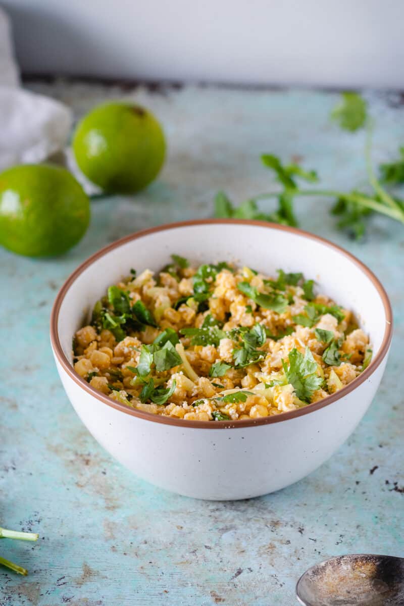 Corn with miso lime butter in a white bowl with limes and cilantro in the background