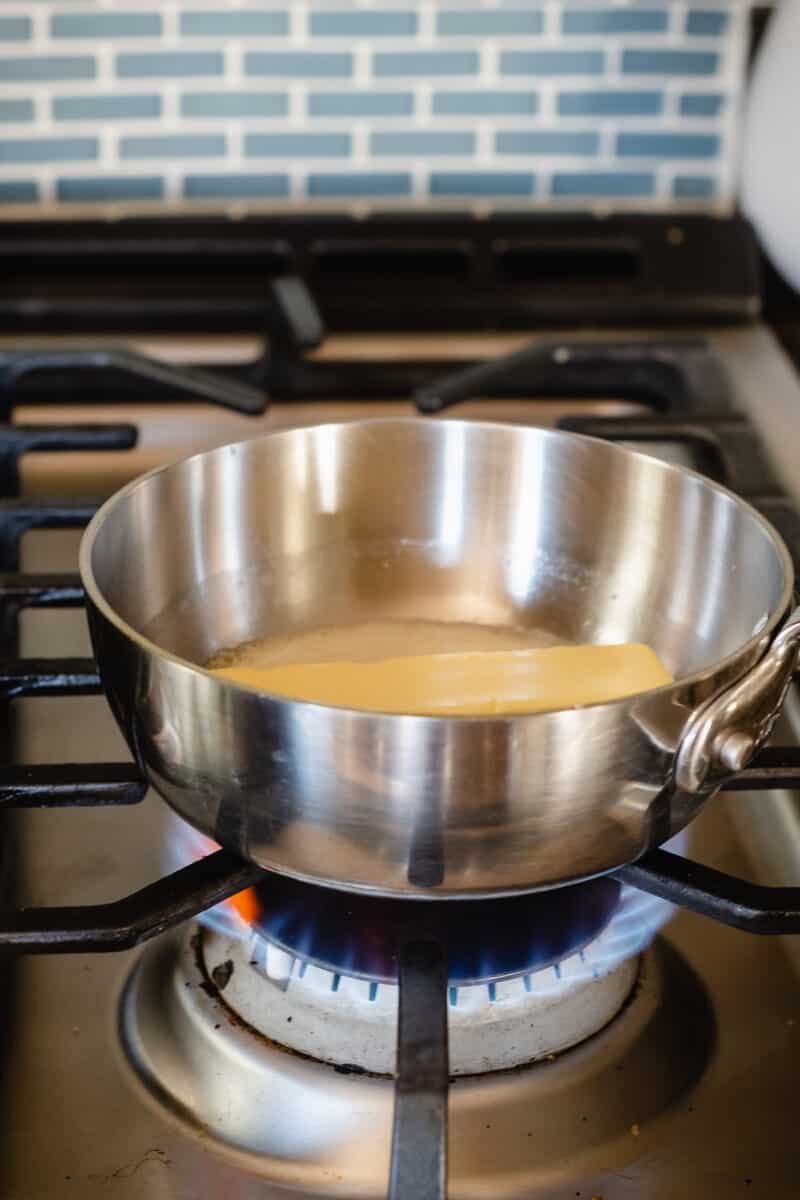 A stick of butter melting in a saucepan on a gas stove burner