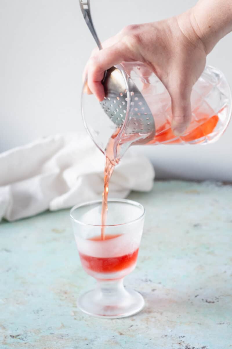 Hand straining a Negroni into a chilled glass through a Julep strainer