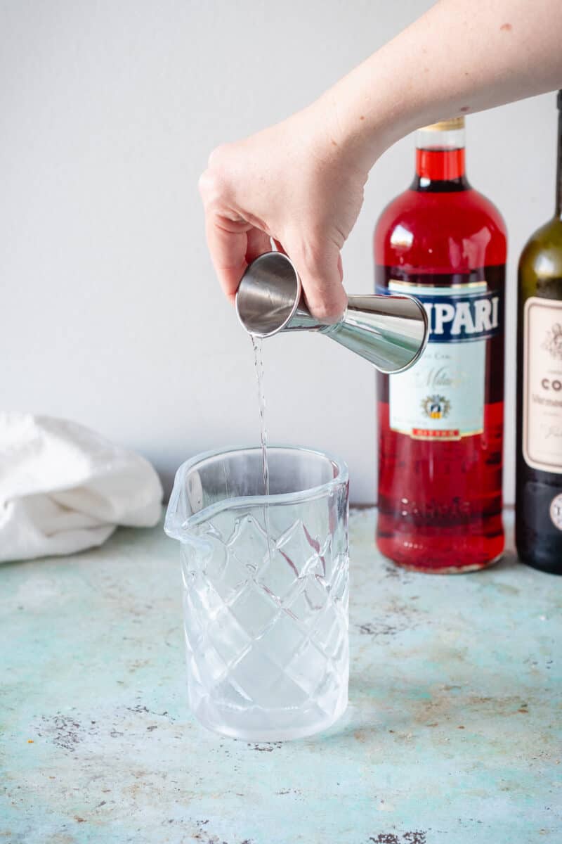 Hand pouring an ounce of gin from a jigger into a mixing glass