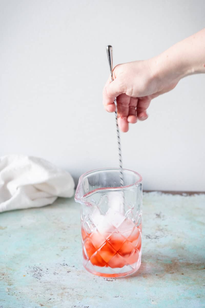 Hand stirring a Negroni in a mixing glass with a long cocktail spoon