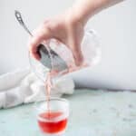 Hand straining Negroni into a footed rocks glass from a mixing glass