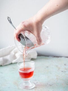 Hand straining Negroni into a footed rocks glass from a mixing glass