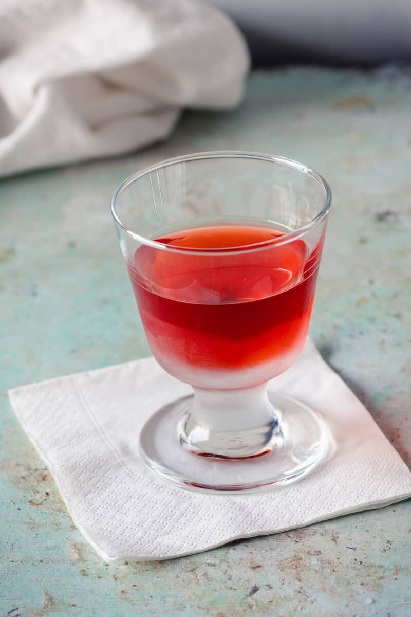 Negroni in a chilled footed rocks glass on a white paper cocktail napkin