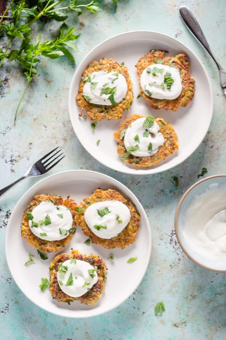 Two plates of zucchini fritters topped with yogurt and mint